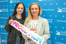 two women smiling - they are standing in front of signs with NWRC on them and holding proud mum