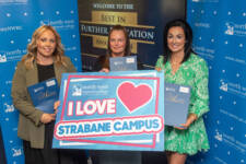 Three women hold a sign that says I love Strabane campus