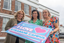 Three women outside a large building holding a big sign that says I love Strabane campus