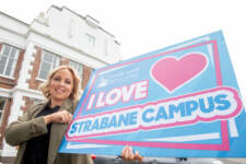 Woman outside a large building holding a big sign that says I love Strabane campus