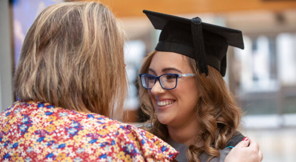 female graduate smiling, while hugging her mother