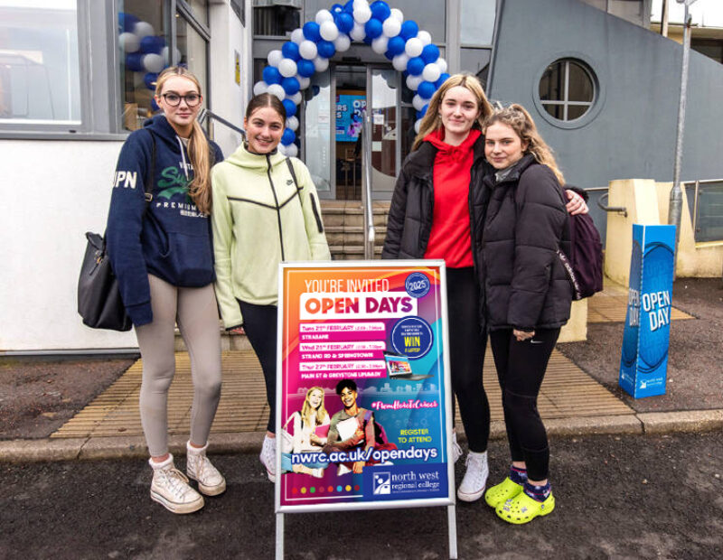 four girls stand outside college building beside Open Day sign