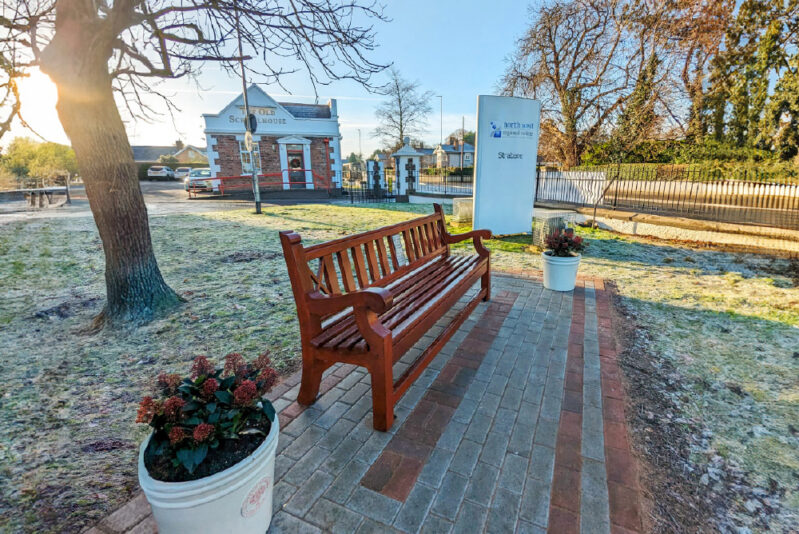 Bench in the foreground with flower pots and sun shining behind the trees