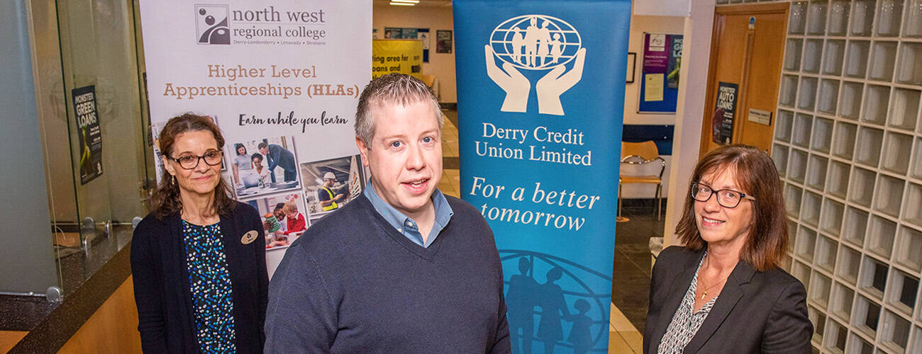 mature male and two females smiling and standing in front of Higher Level Apprenticeship pop-up stand in Derry City union pop-up