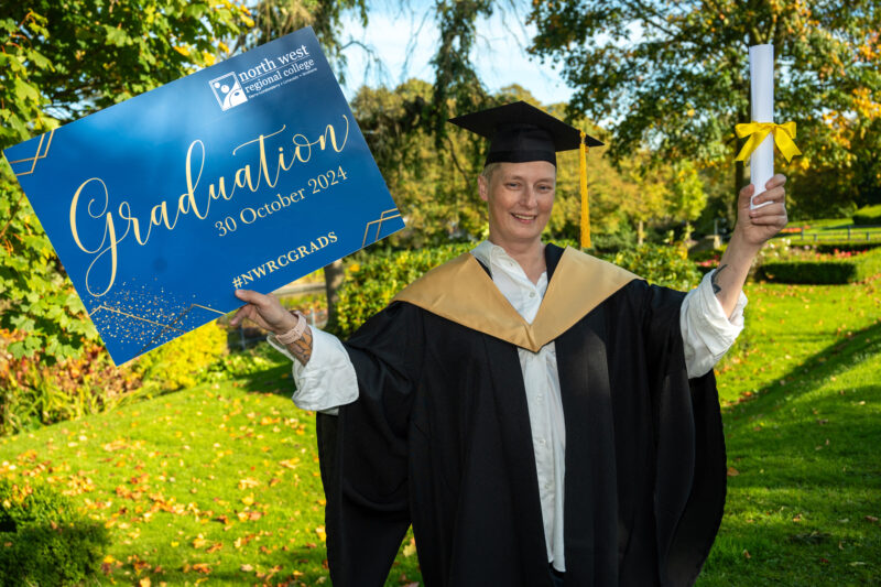 Woman in a graduation gown and hat holding a graduation sign