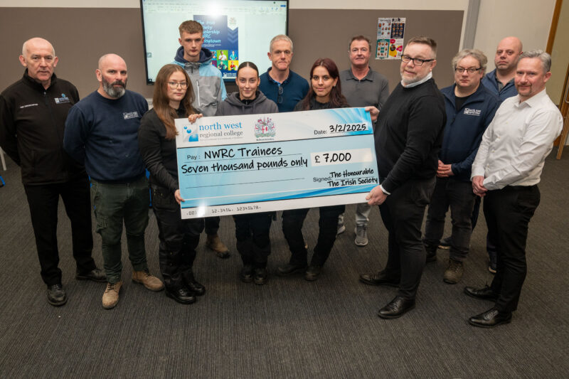 group of ten people in a classroom holding a cheque made out to trainees for £1,000