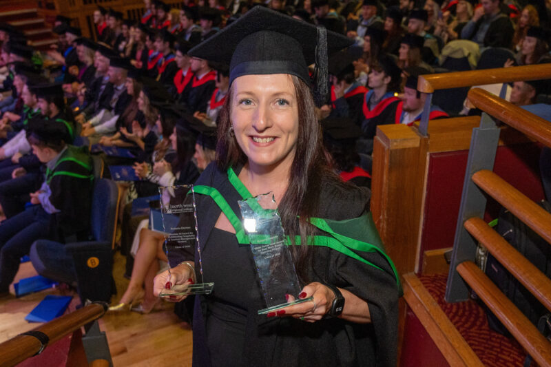 women in graduation gown holding a trophy