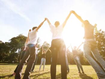 People holding hands in a field with the sun shining through