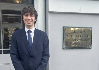 man in a suit standing outside an office with a gold plate that states McDaid, McCullough and Moore.