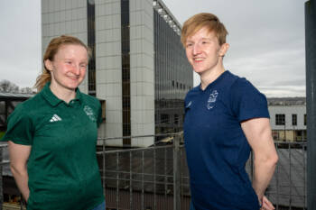 Two Athletes in a green and navy t-short outside the college buildings