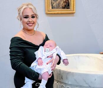 woman holding a baby in front of a baptismal font